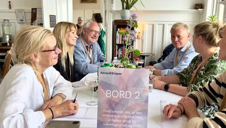 Seks mennesker i samtale omkring bord