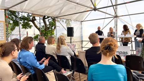 Paneldebat under gennemsigtig teltdug med fire kvinder i panelet. Forrest stolerækker med publikum.