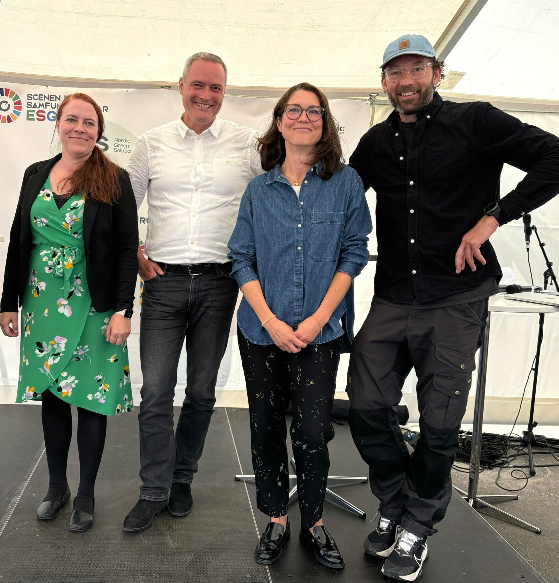 To kvinder og to mænd ved siden af hinanden på scene i stort, lyst telt