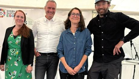 To kvinder og to mænd ved siden af hinanden på scene i stort, lyst telt