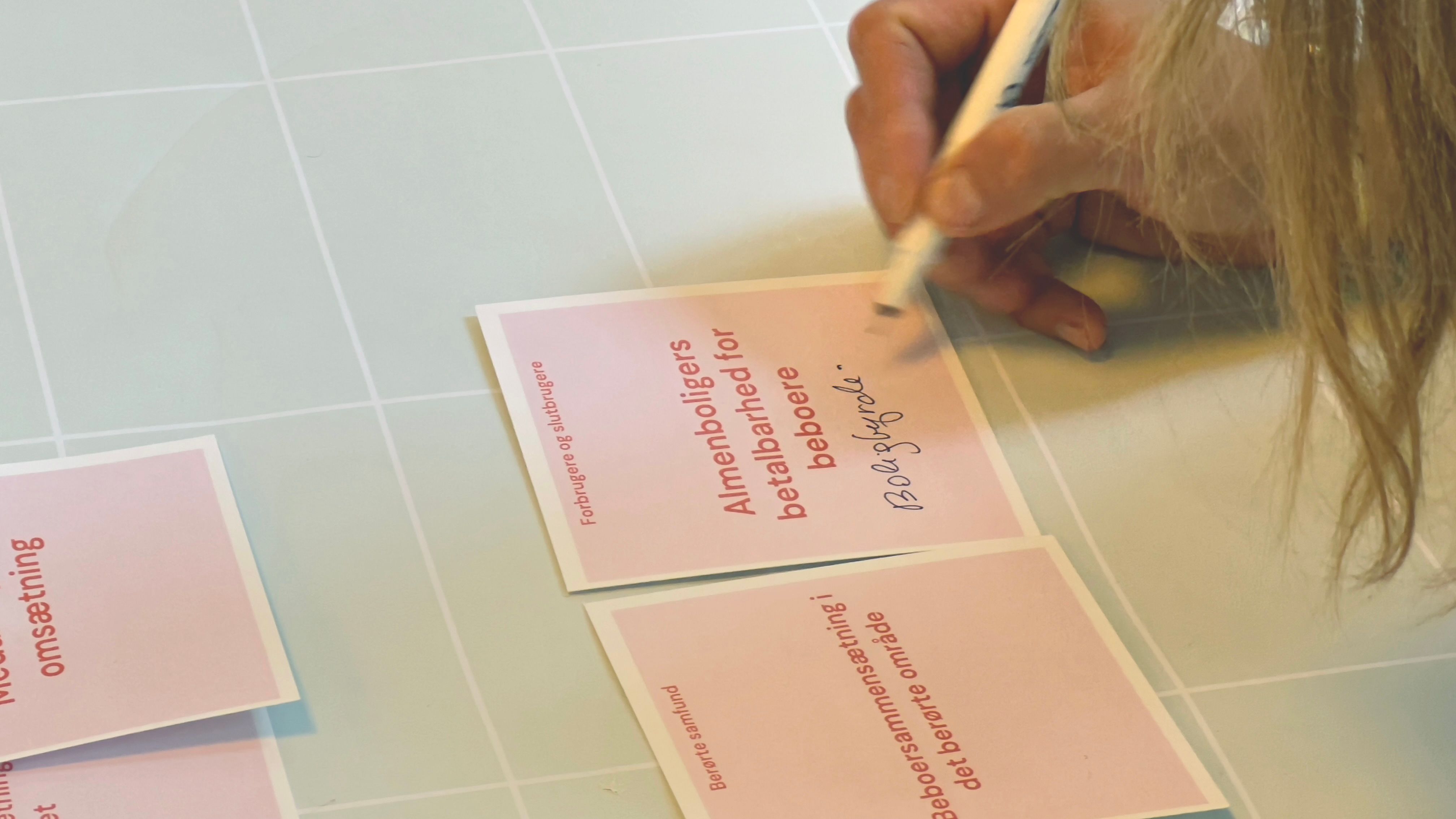 Closeup af hånd der skriver på lyserød, kvadratisk seddel.