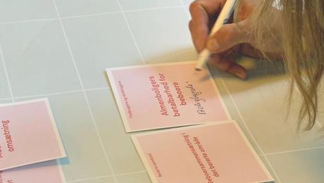 Closeup af hånd der skriver på lyserød, kvadratisk seddel.