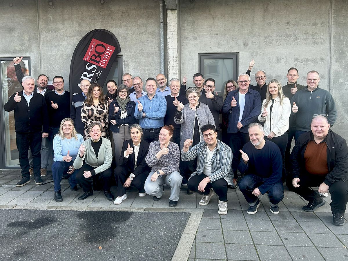 Gruppefoto af 25-30 smilende mennesker uden for bygning