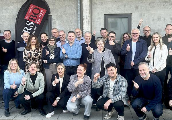 Gruppefoto af 25-30 smilende mennesker uden for bygning