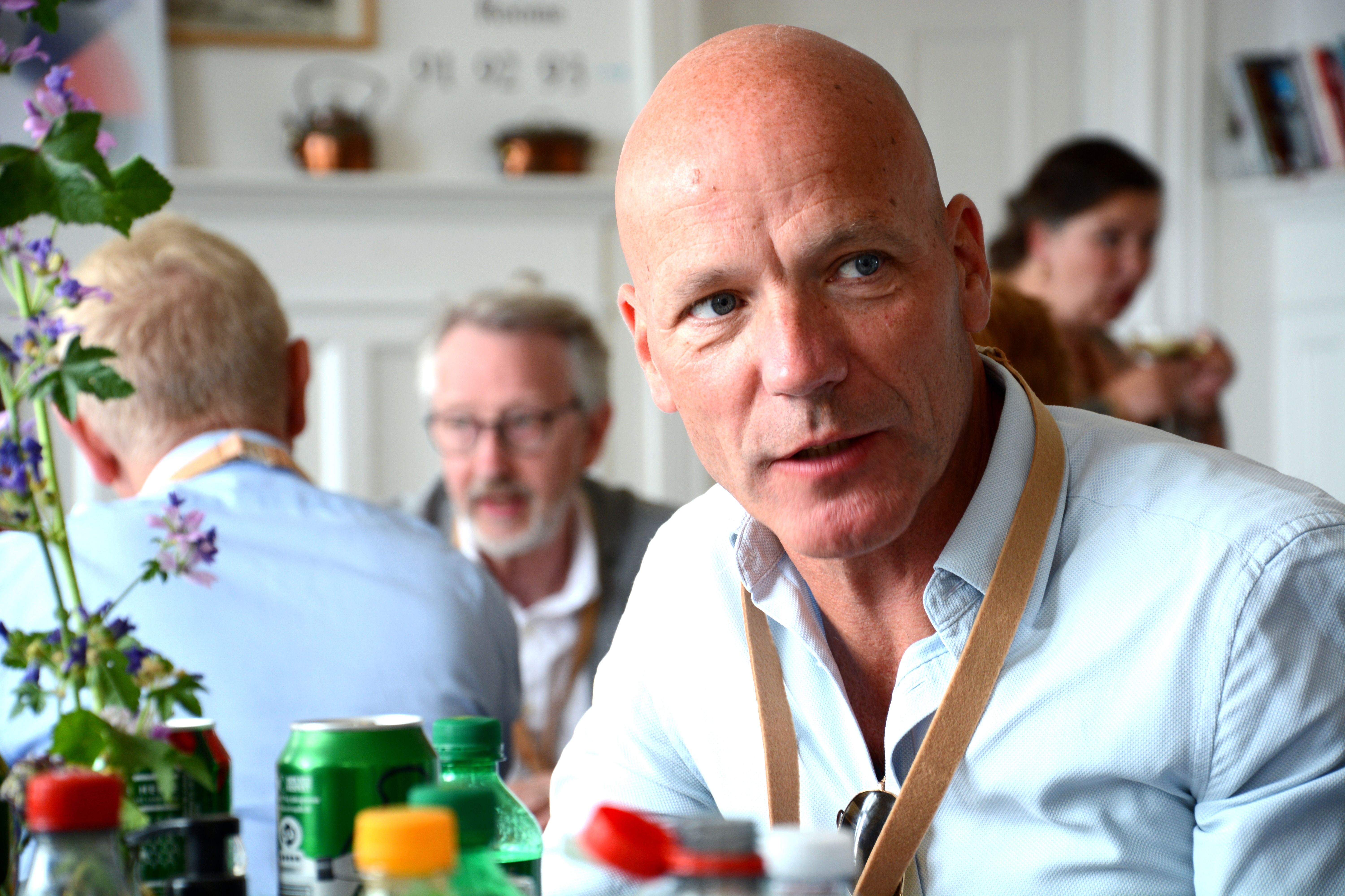 Mand i lyseblå skjorte sidder og lytter i restaurant med mange mennesker