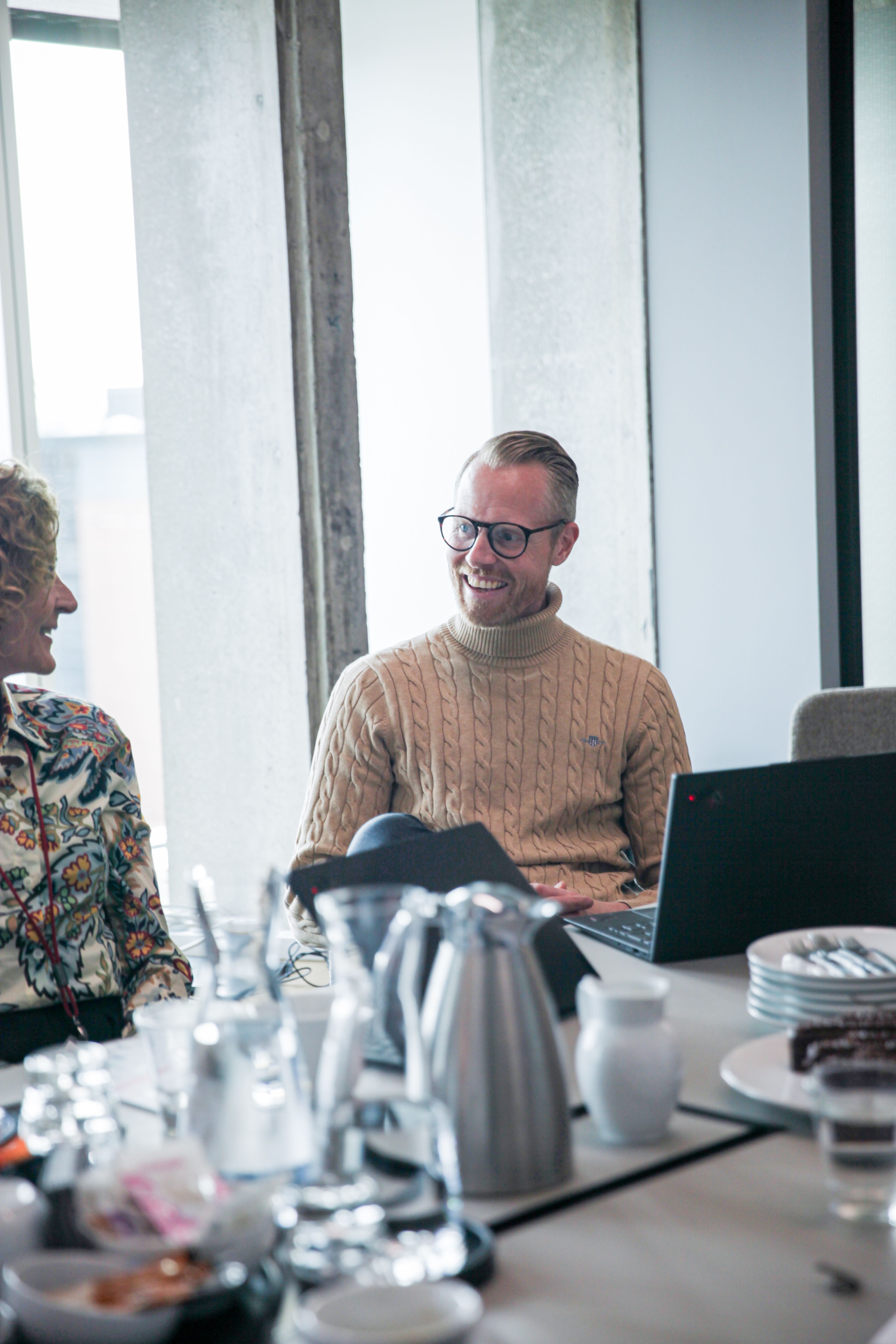 Mand og kvinde ved mødebord smiler til hinanden.