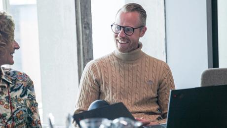 Mand og kvinde ved mødebord smiler til hinanden.