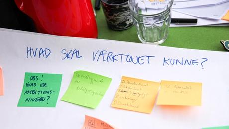 Planche med farverige post-it-noter og en overskrift, hvor der står "Hvad skal værktøjet kunne!"