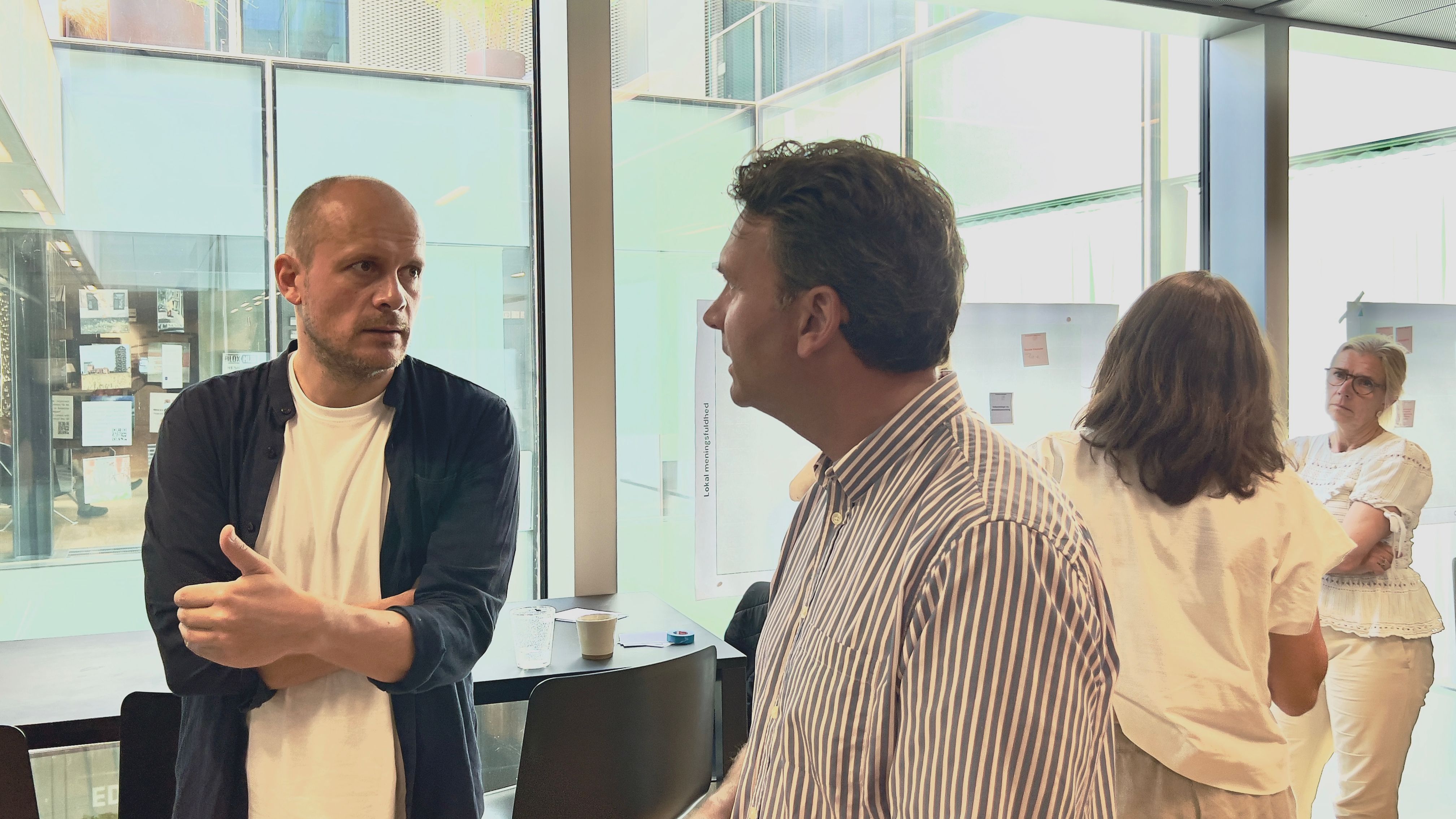 To mænd stående i samtale og to kvinder i baggrunden