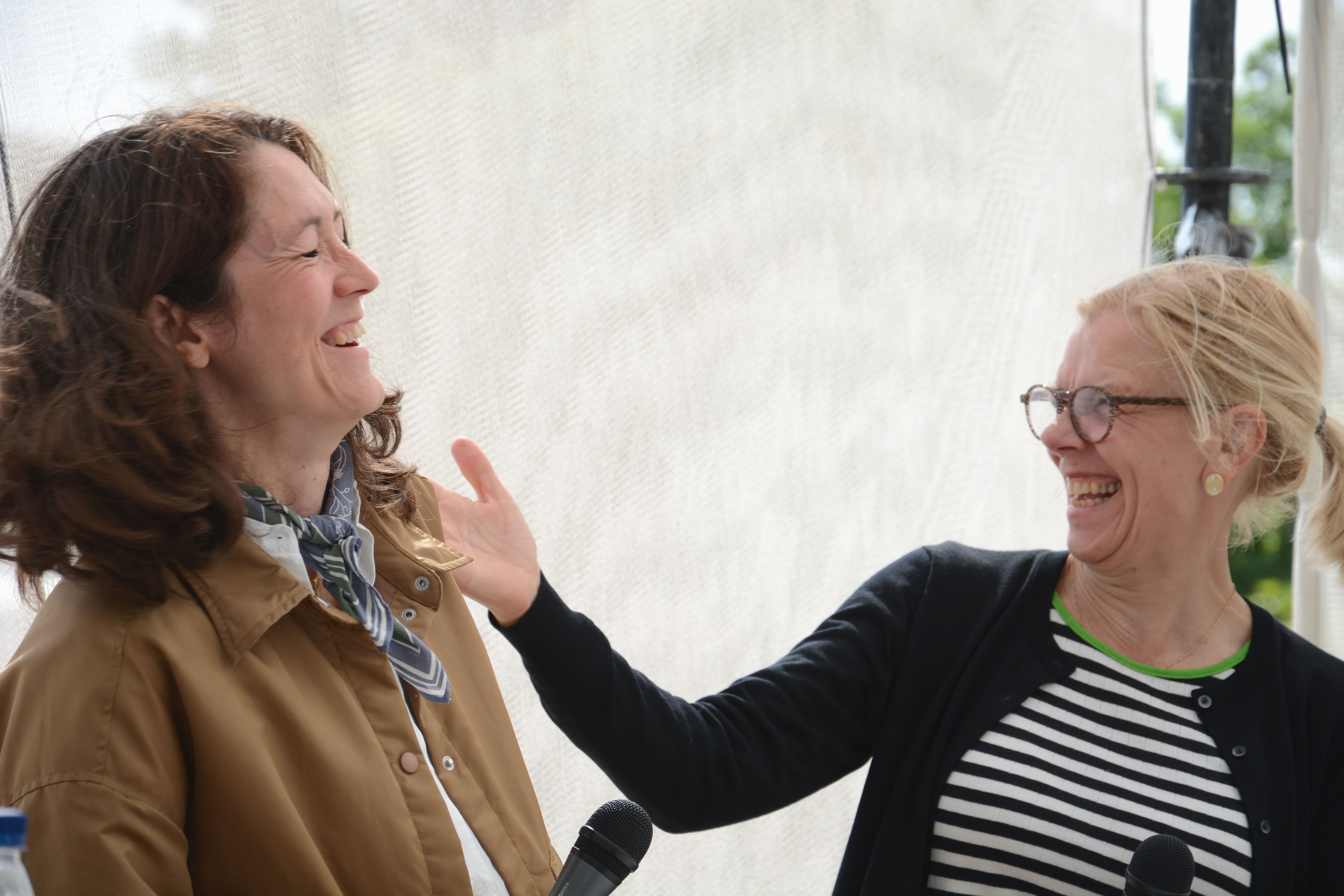 To kvinder med mikrofoner griner og gestikulerer til hinanden