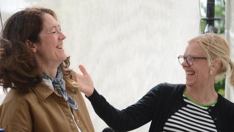 To kvinder med mikrofoner griner og gestikulerer til hinanden