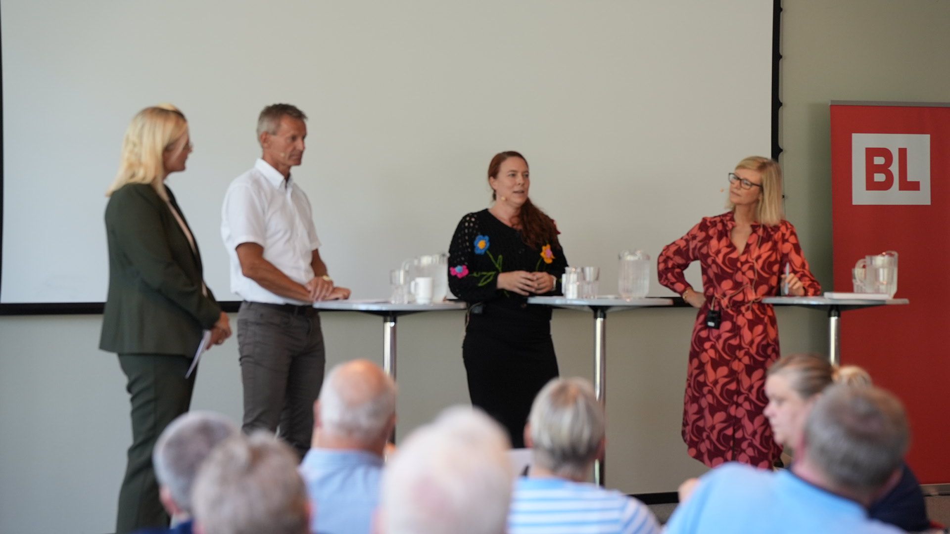 Fire mennesker på en scene med BL-logo på roll-up i siden