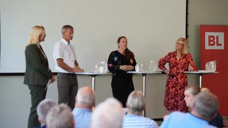 Fire mennesker på en scene med BL-logo på roll-up i siden