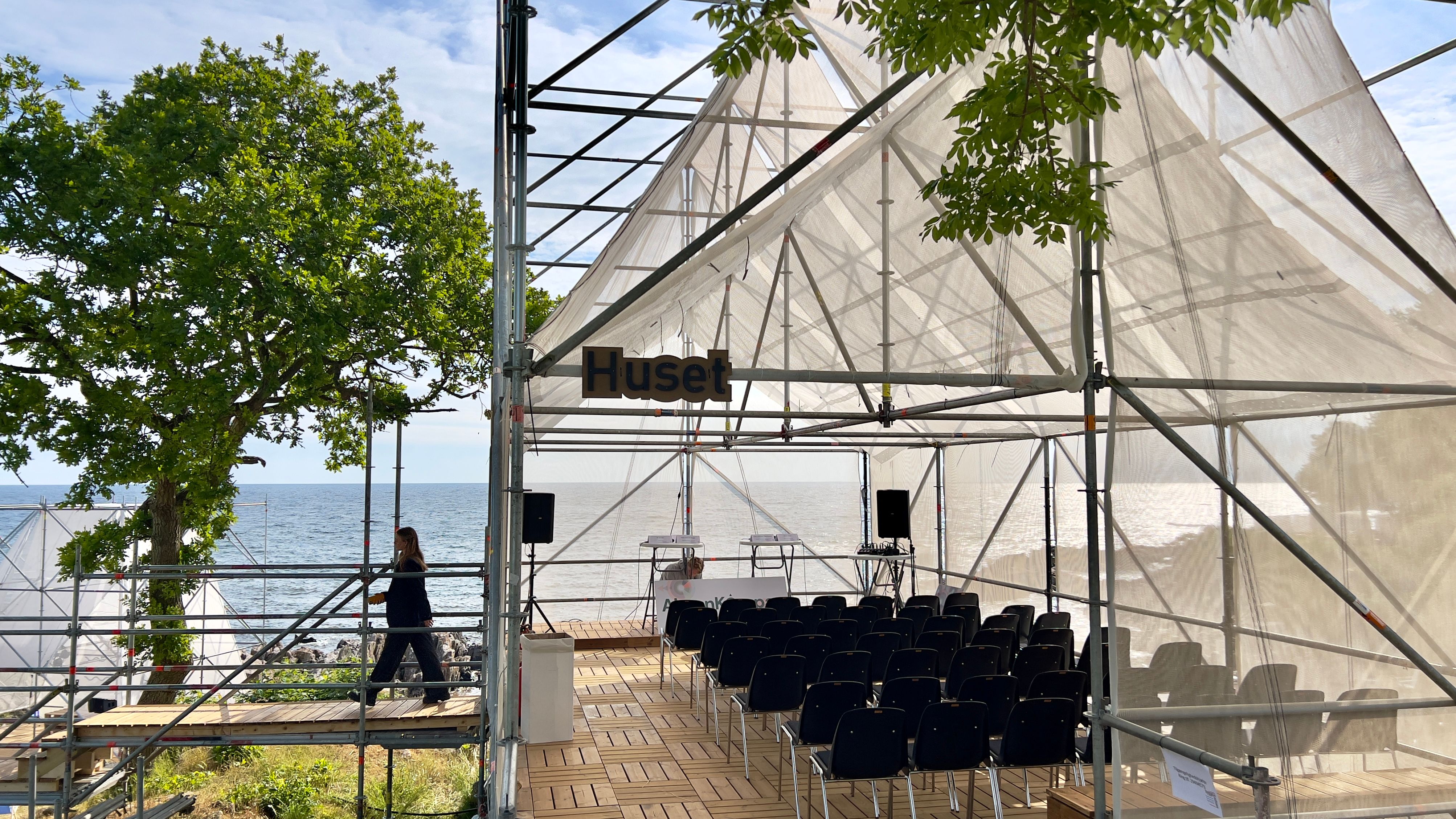 Debattelt med stolerækker under teltdug med udsigt til vand