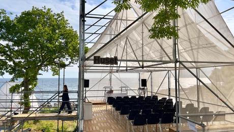 Debattelt med stolerækker under teltdug med udsigt til vand