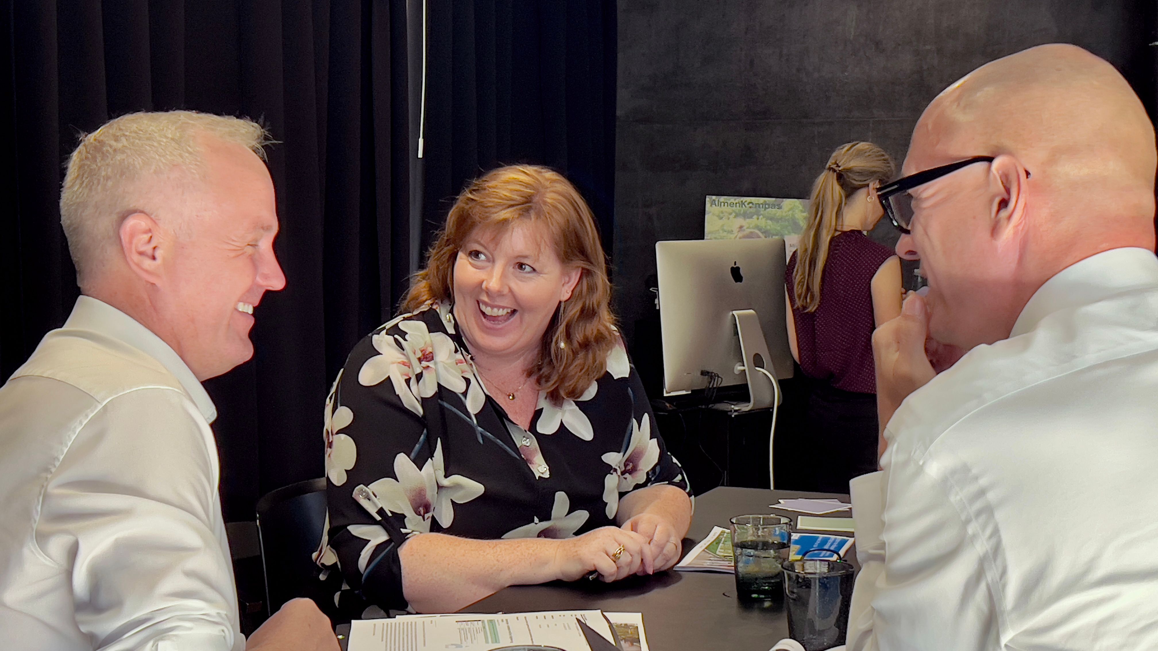 To mænd og en kvinde sidder ved bord og griner