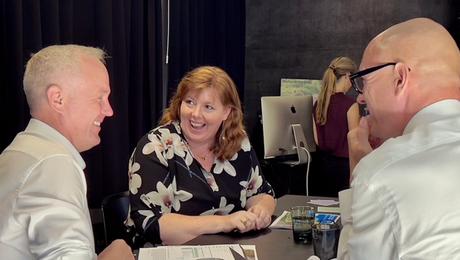 To mænd og en kvinde sidder ved bord og griner