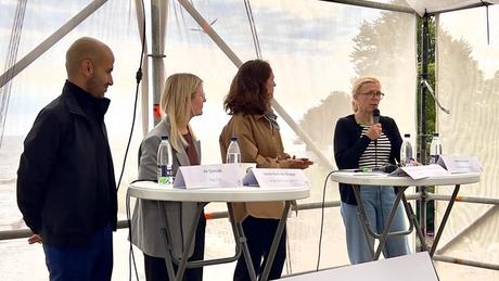 Tre kvinder og en mand står ved høje borde i paneldebat i telt.