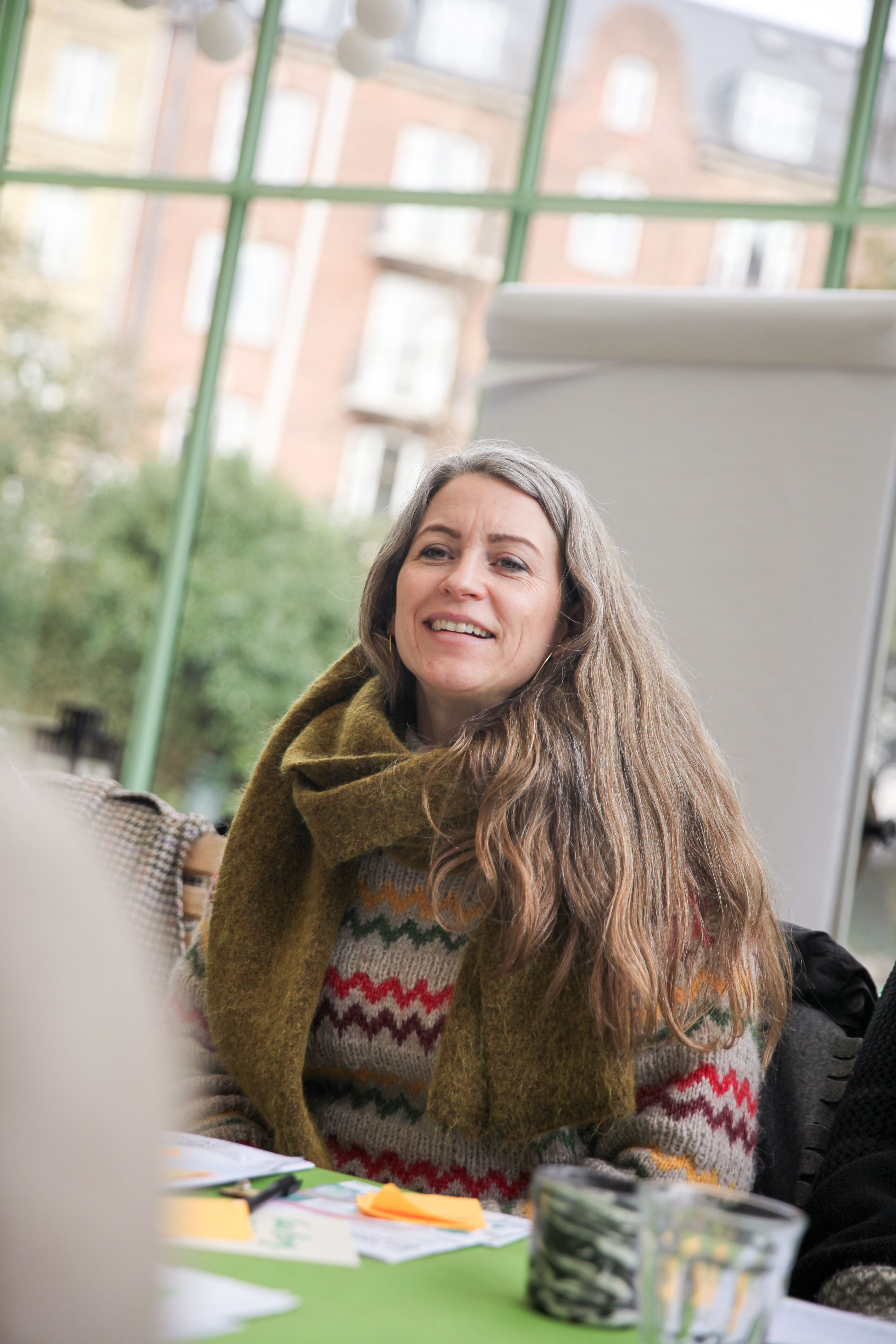 Kvinde siddende i café med store ruder og flip-over bag sig og post-it-sedler og papirer på bordet foran sig