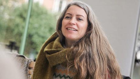 Kvinde siddende i café med store ruder og flip-over bag sig og post-it-sedler og papirer på bordet foran sig