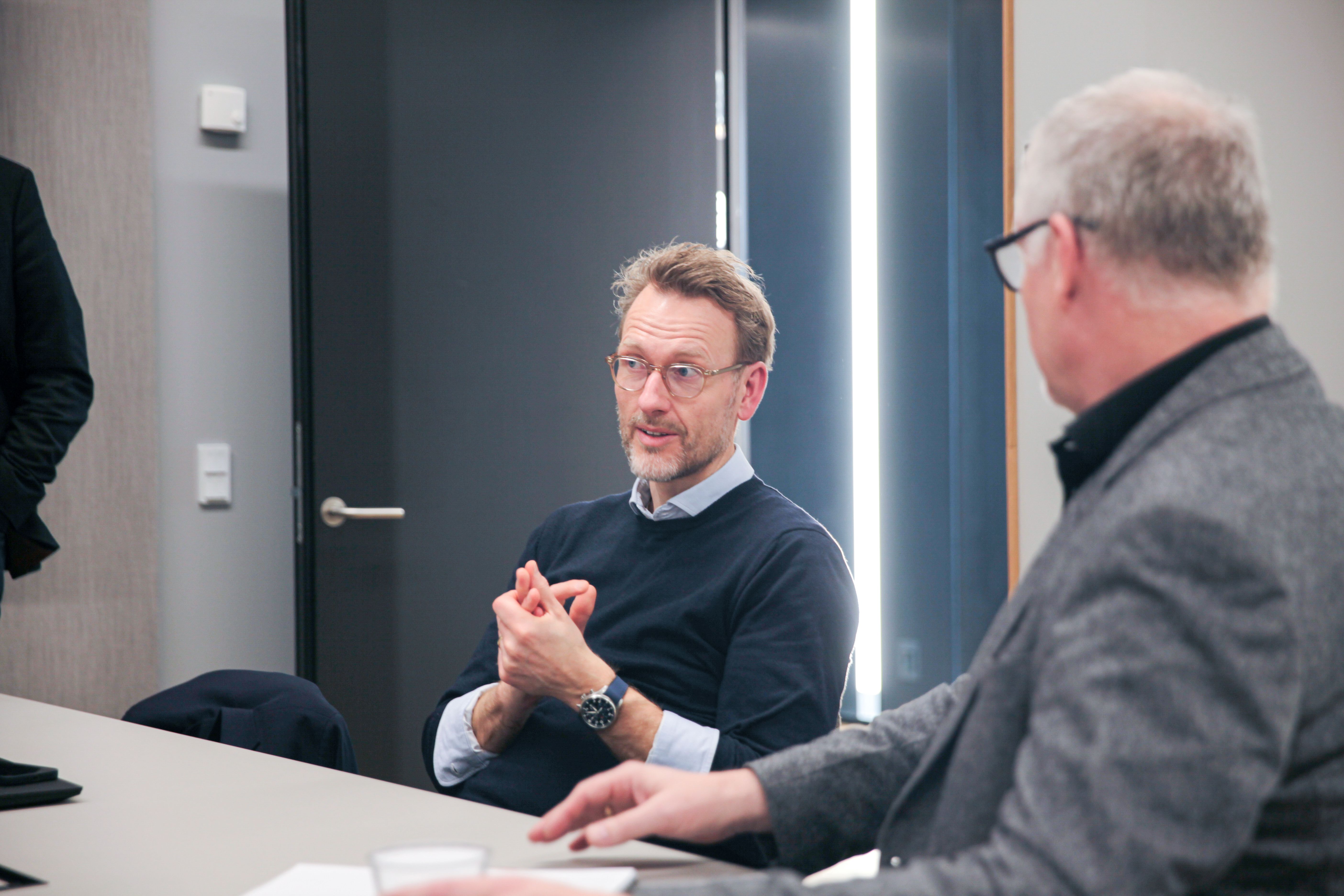 To mænd ved bord i mødelokale. En taler, mens den anden lytter 