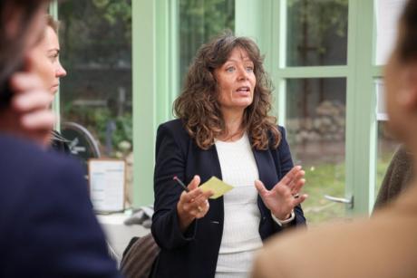 Kvinde står og taler med en kuglepen og en post-it med fire tilhørere omkring sig.