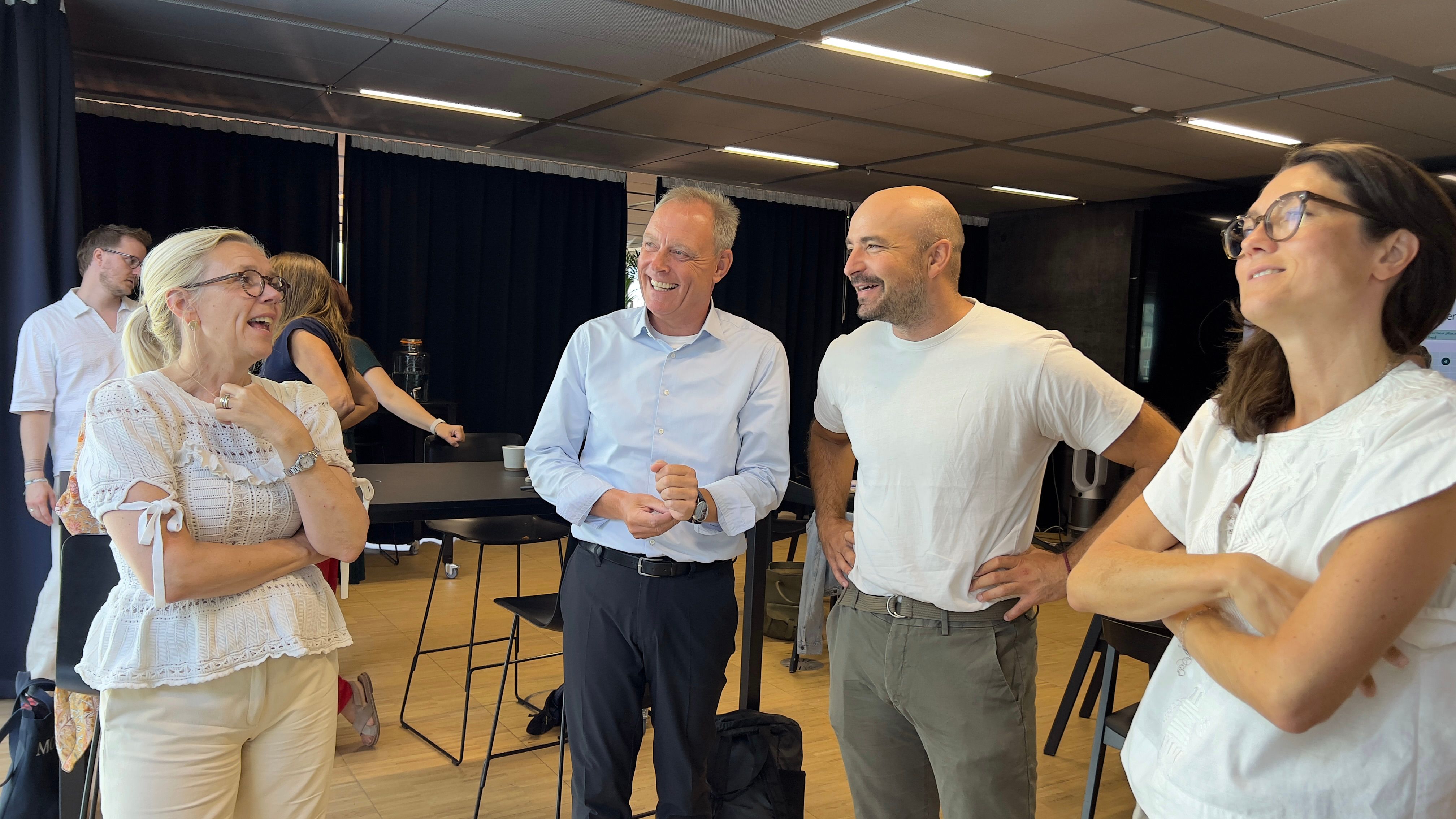 To mænd og to kvinder i mødelokale står og griner