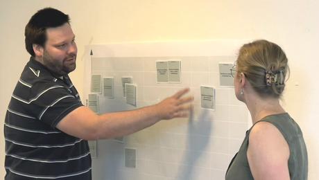 En mand og en kvinde peger på og drøfter sedler placeret på en væg