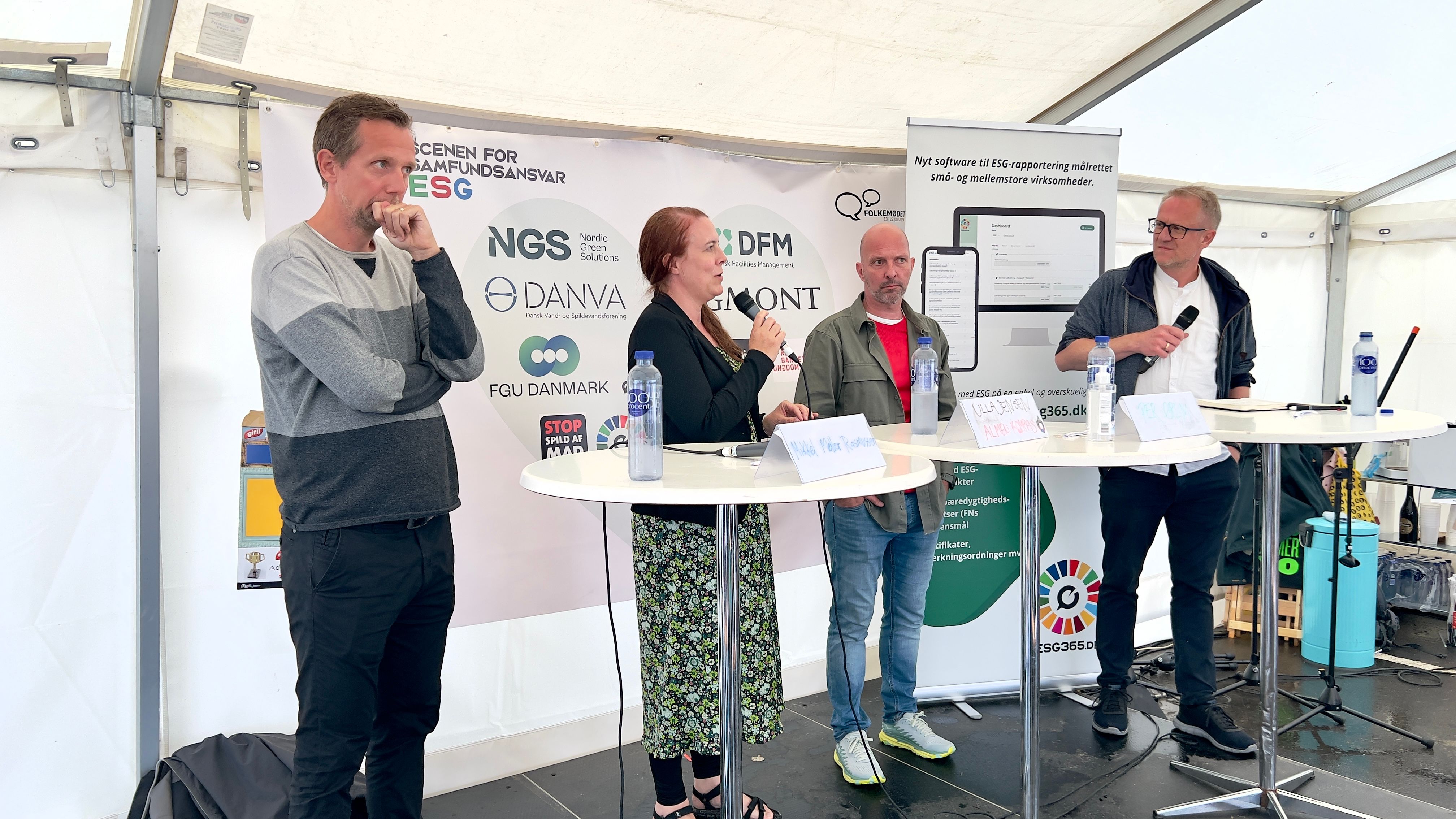 Paneldebat i stort hvidt telt. En kvinde taler i mikrofon omgivet af tre mænd