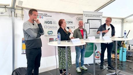 Paneldebat i stort hvidt telt. En kvinde taler i mikrofon omgivet af tre mænd