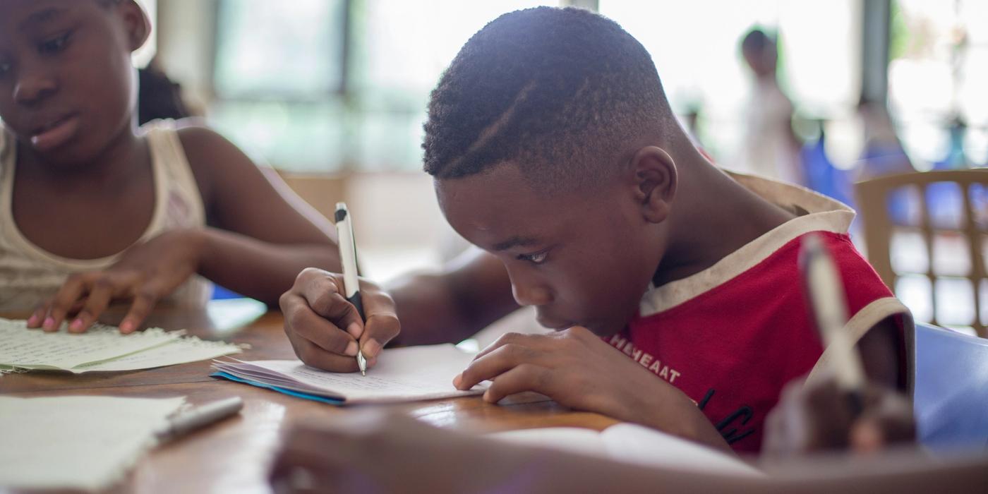 A young student sitting alone at a desk in a public school classroom in St. Petersburg, looking out a window in afternoon light