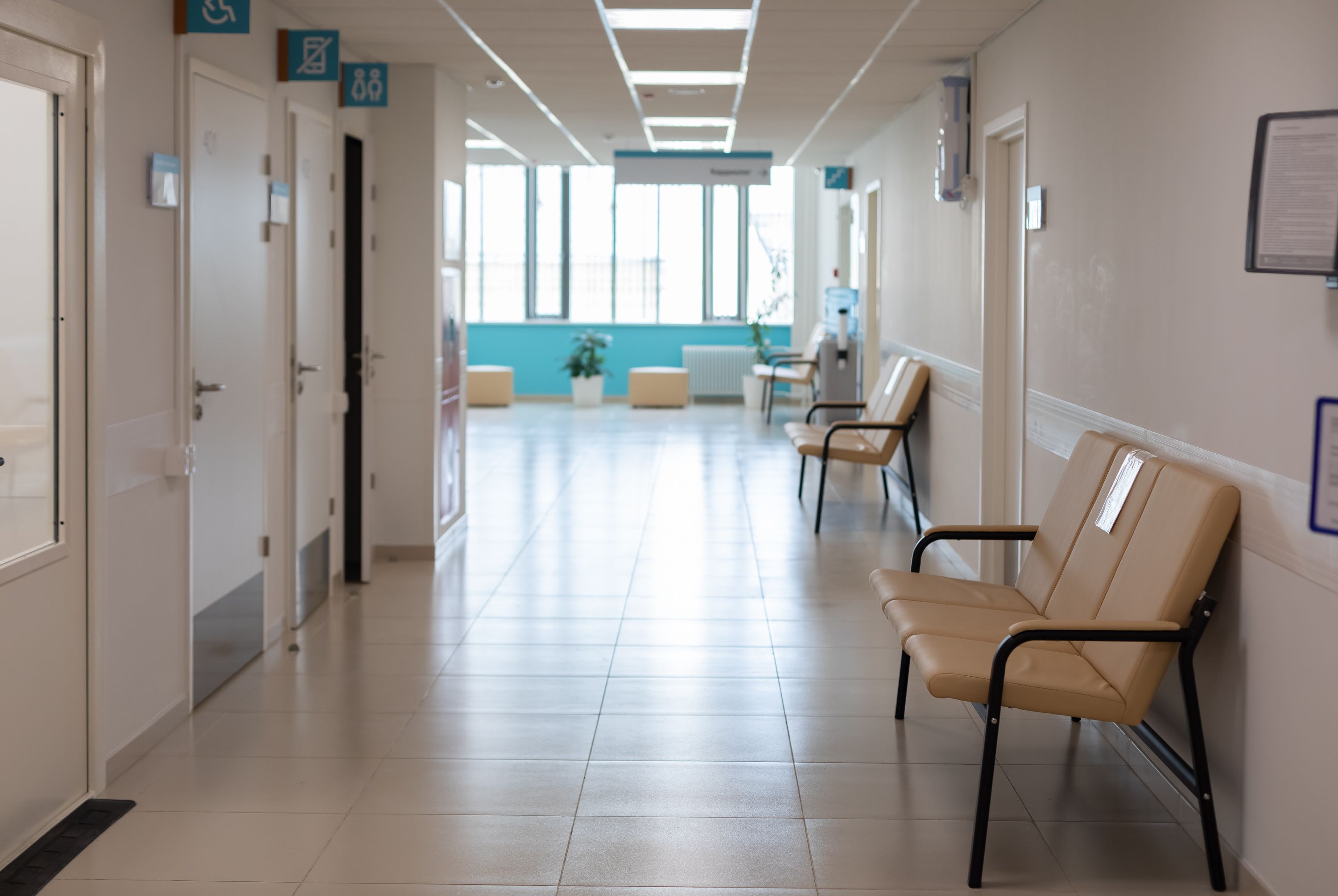Empty hospital corridor with seating along the wall and patient rooms.