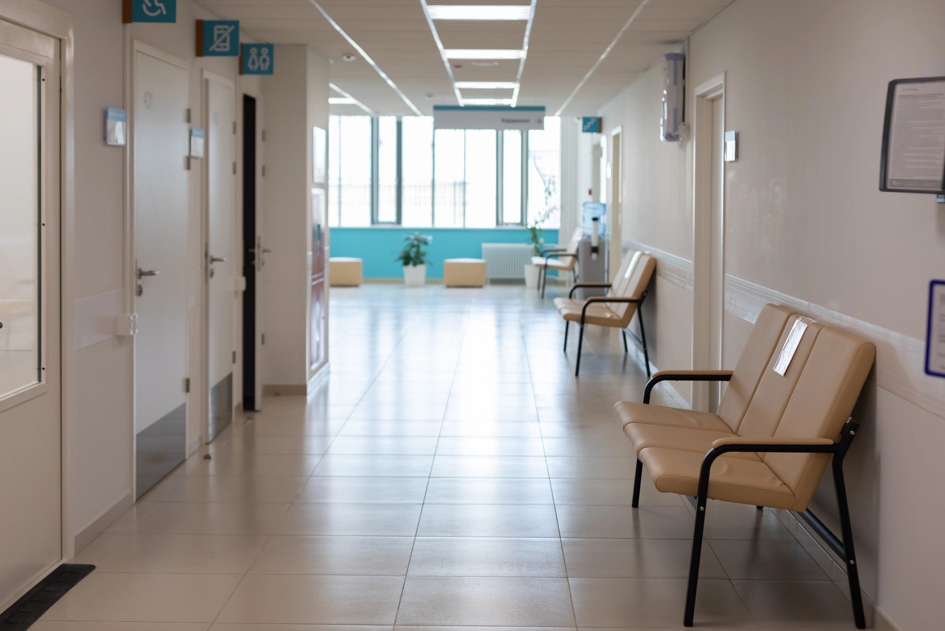 Empty hospital corridor with seating along the wall and patient rooms.