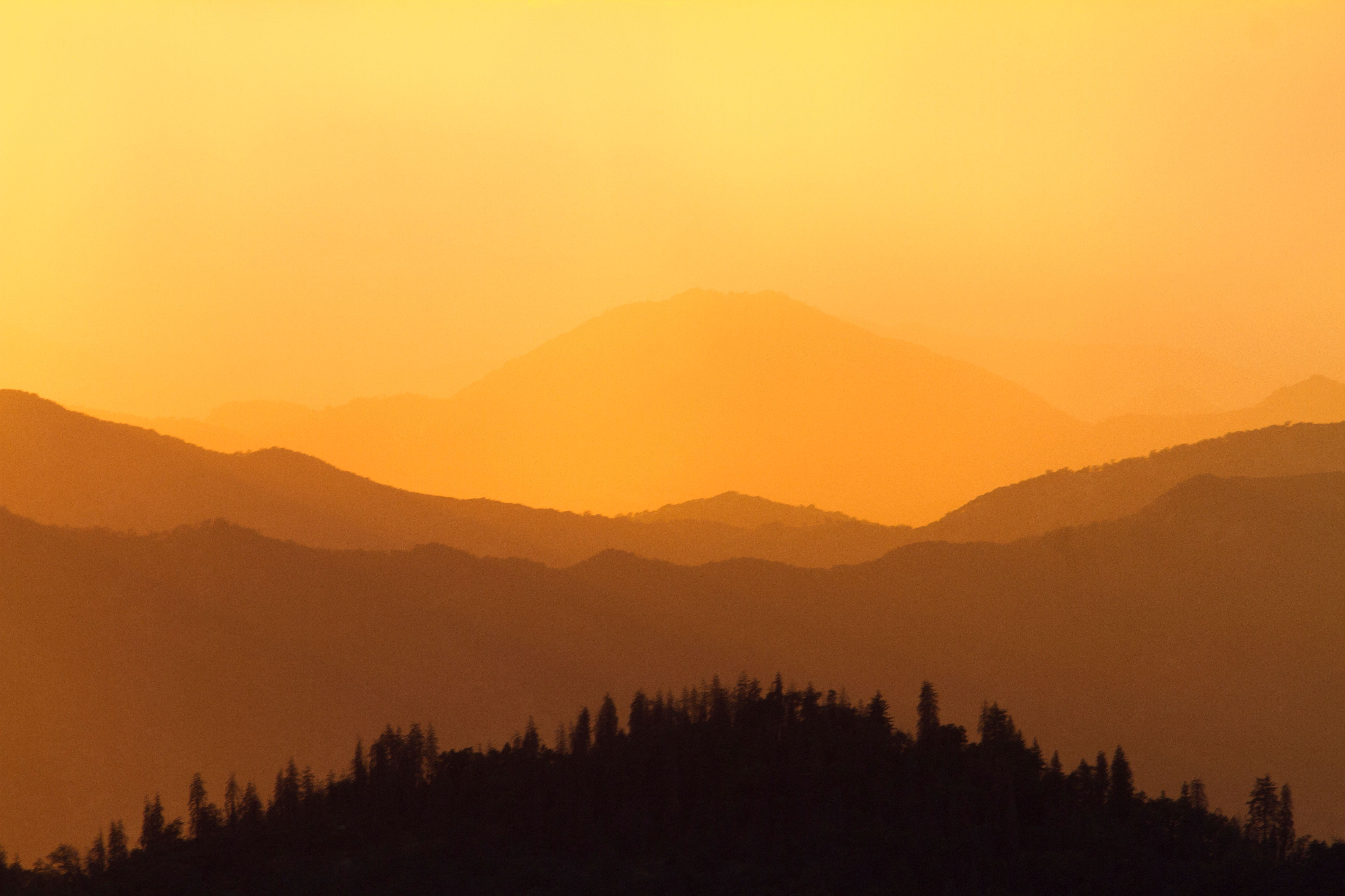 Layered mountain ridges silhouetted against an orange sunset sky.