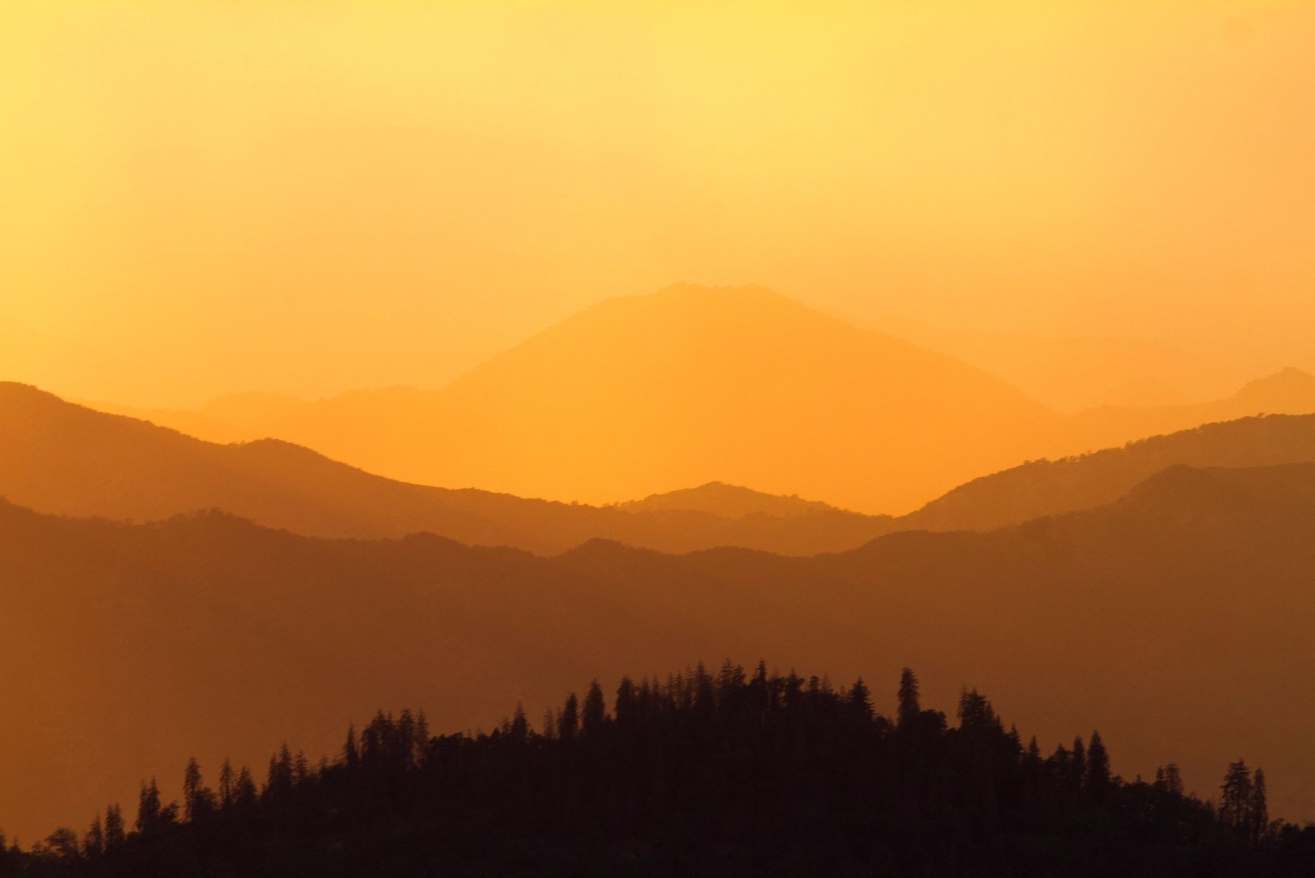 Layered mountain ridges silhouetted against an orange sunset sky.