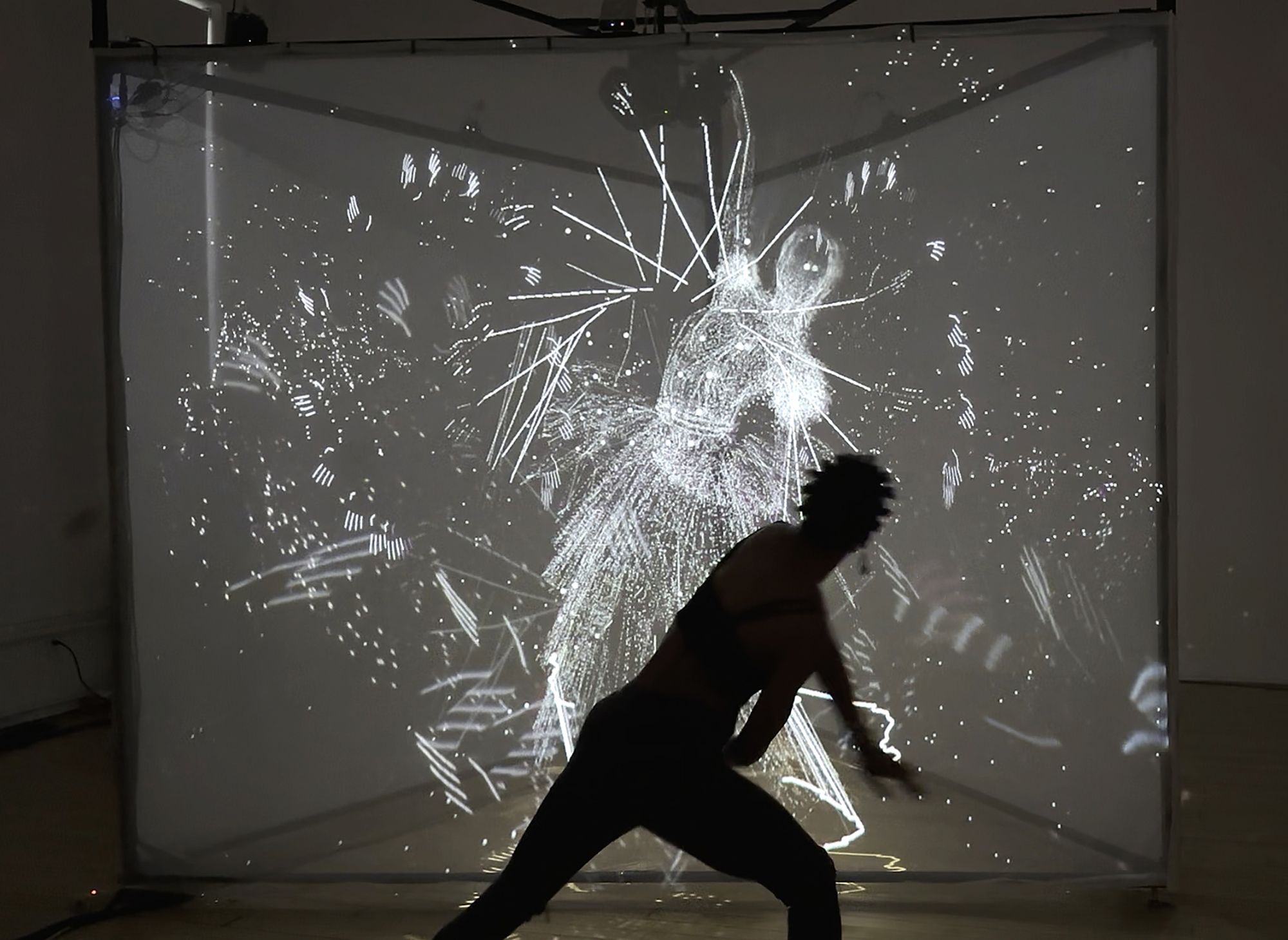 A silhouetted figure moves in front of a glowing projection of abstract, motion-reactive visuals forming a ghostly human shape.