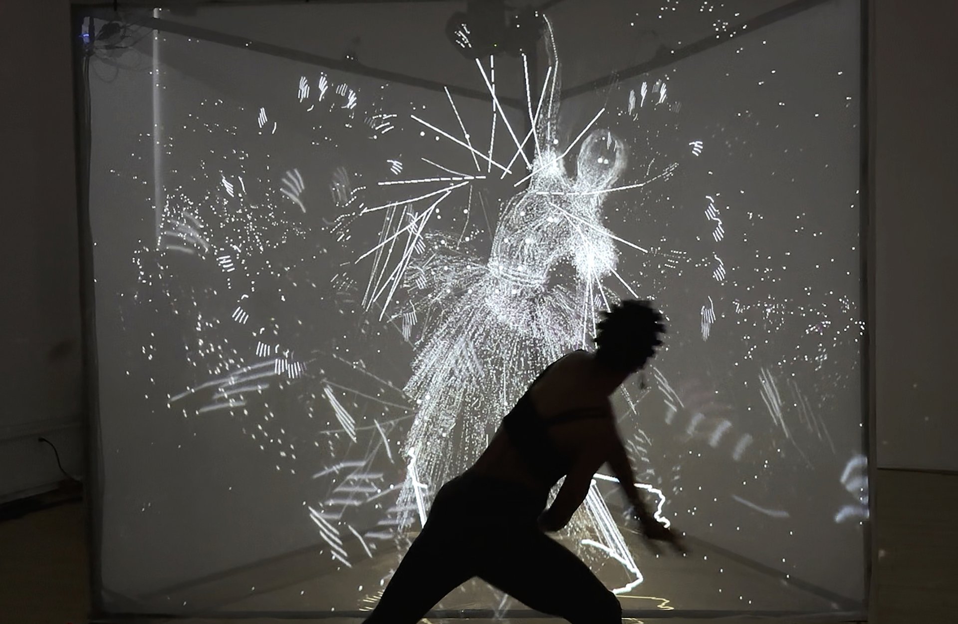 A silhouetted figure moves in front of a glowing projection of abstract, motion-reactive visuals forming a ghostly human shape.