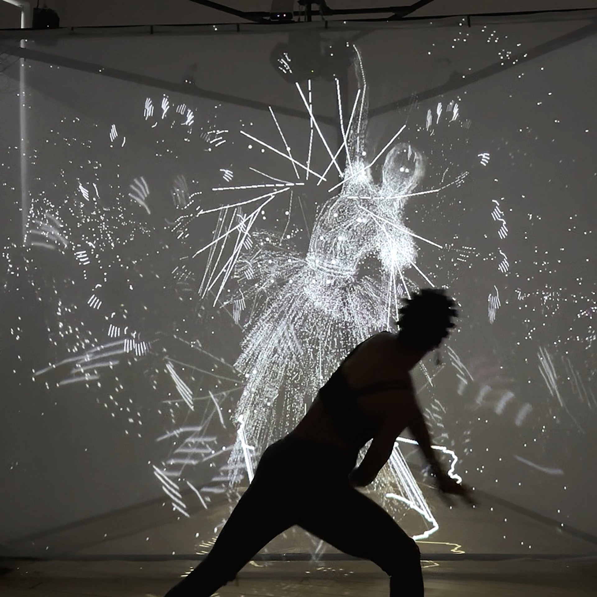 A silhouetted figure moves in front of a glowing projection of abstract, motion-reactive visuals forming a ghostly human shape.