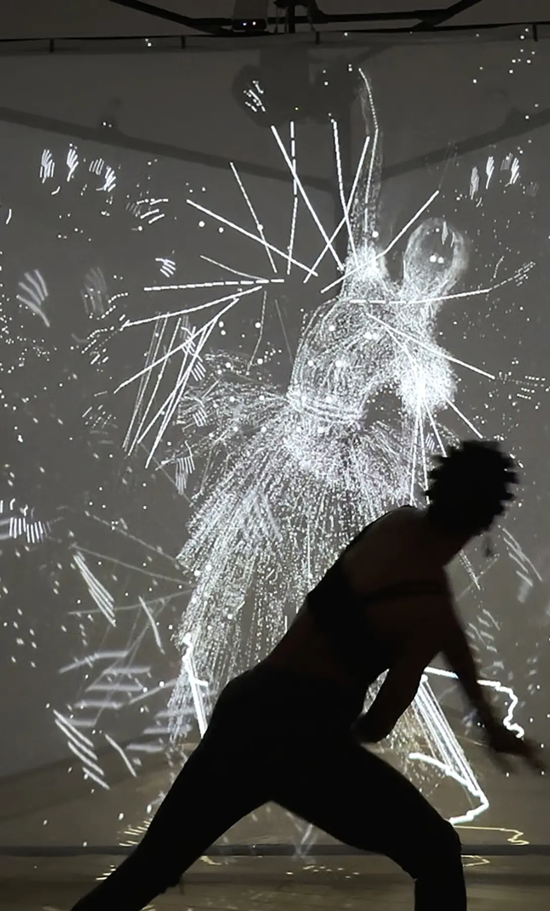 A silhouetted figure moves in front of a glowing projection of abstract, motion-reactive visuals forming a ghostly human shape.