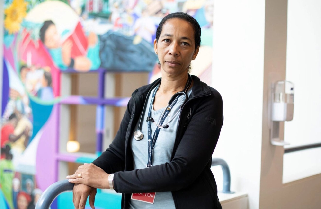 Healthcare provider with a stethoscope stands in a hospital hallway in front of a colorful mural.