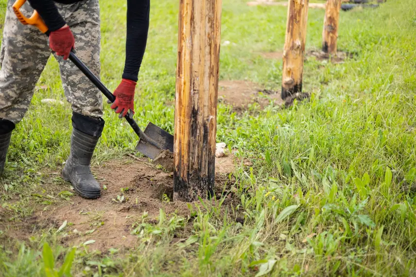 Person digging beside wooden posts in grass.