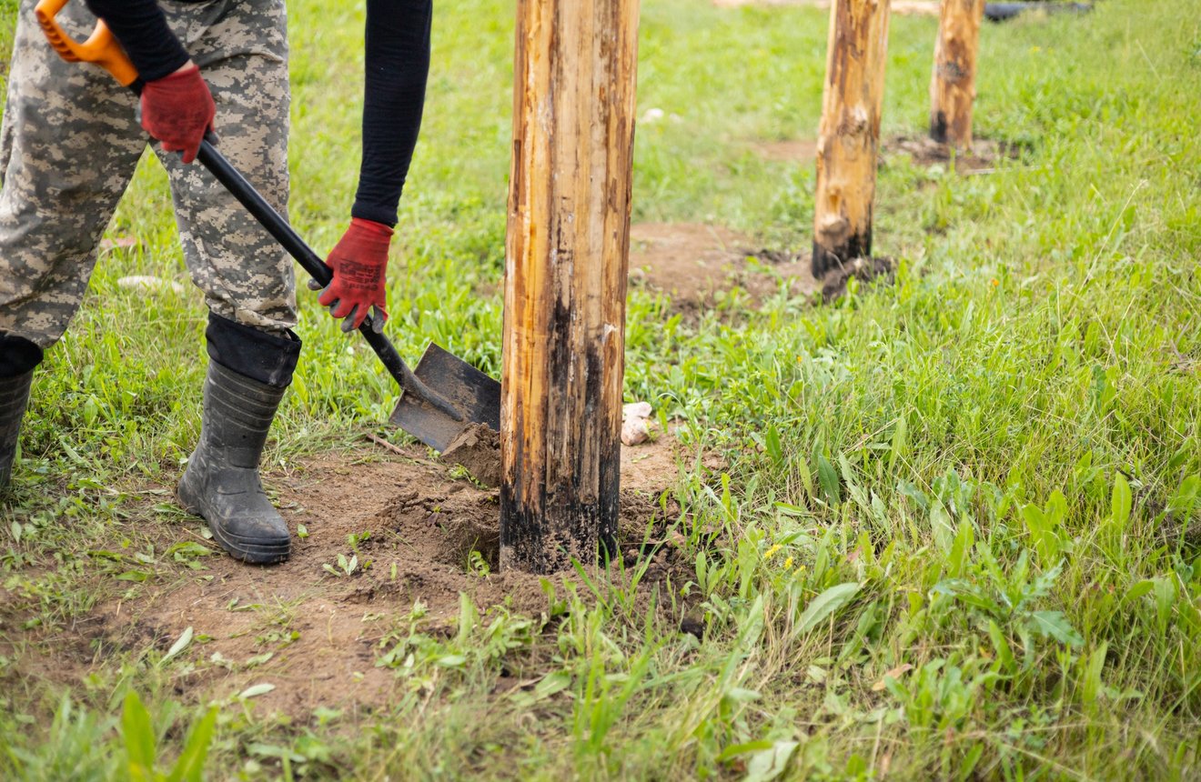 Person digging beside wooden posts in grass.