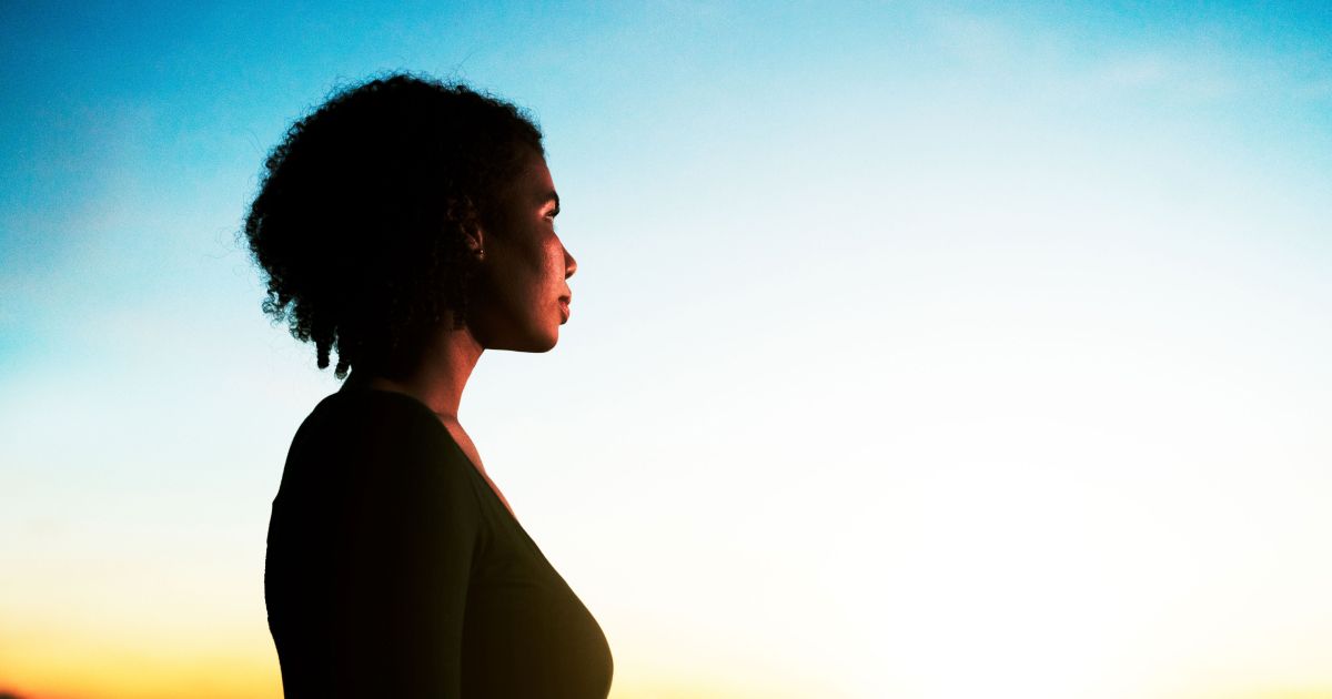 Woman in profile looking into the distance during golden hour or sunrise.