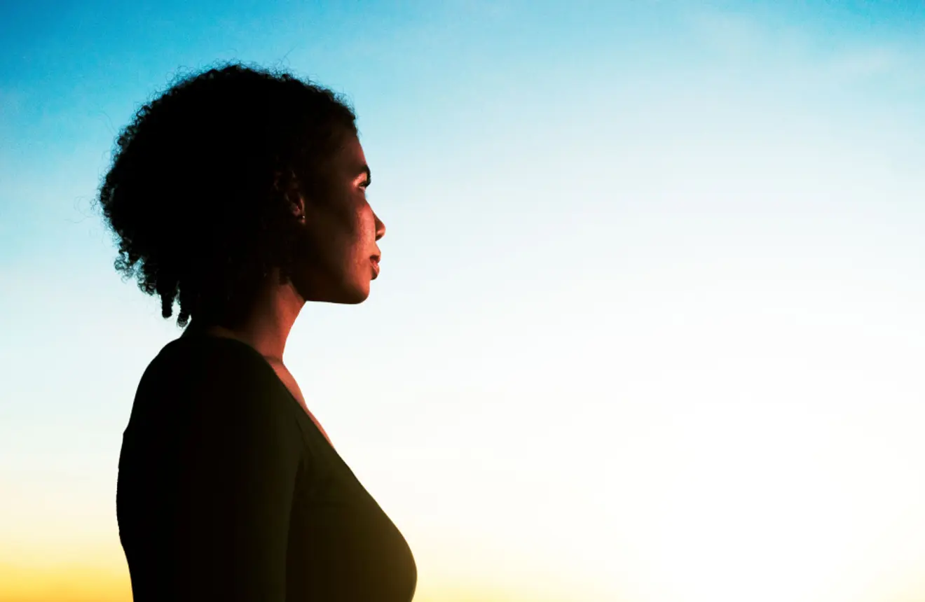 Woman in profile looking into the distance during golden hour or sunrise.