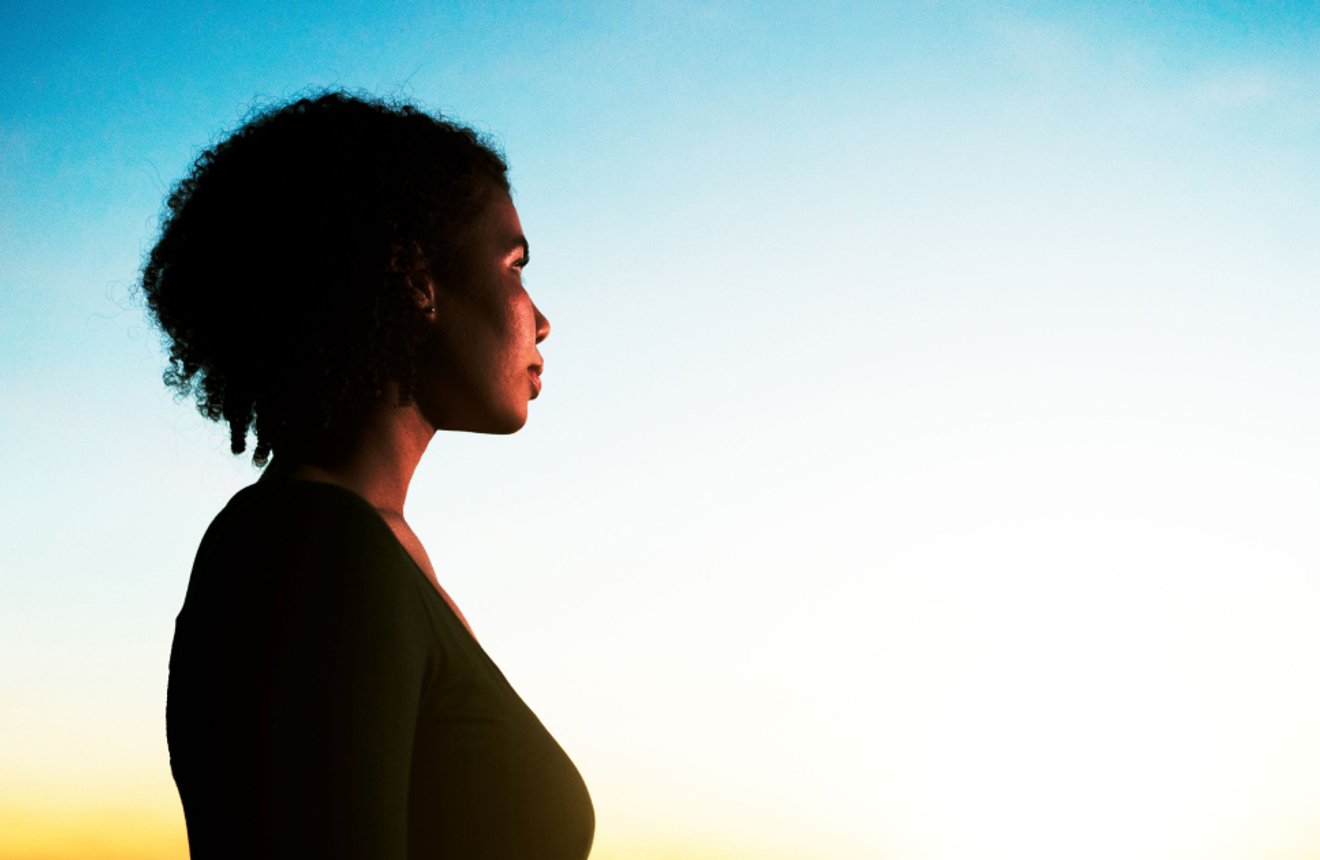 Woman in profile looking into the distance during golden hour or sunrise.
