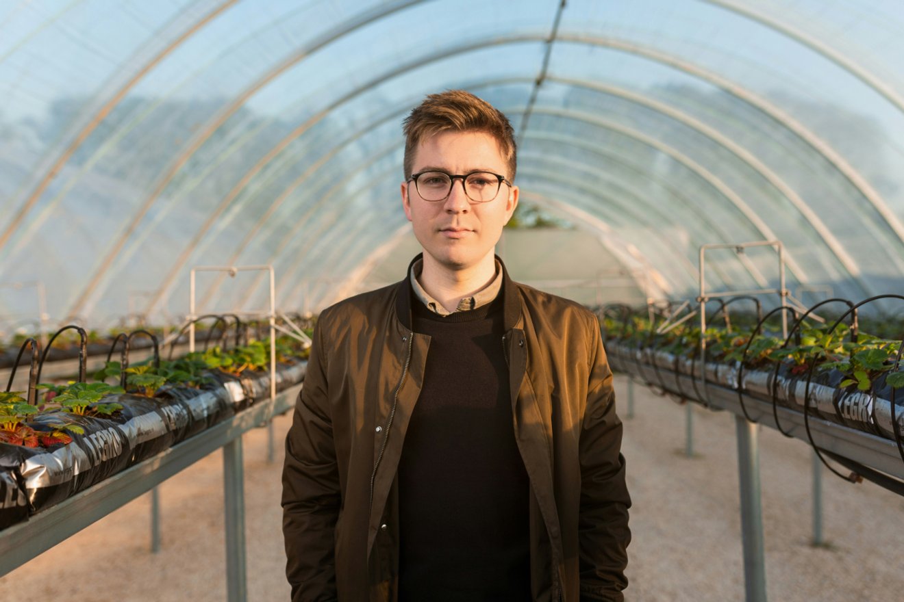 Person standing in a greenhouse with rows of plants.