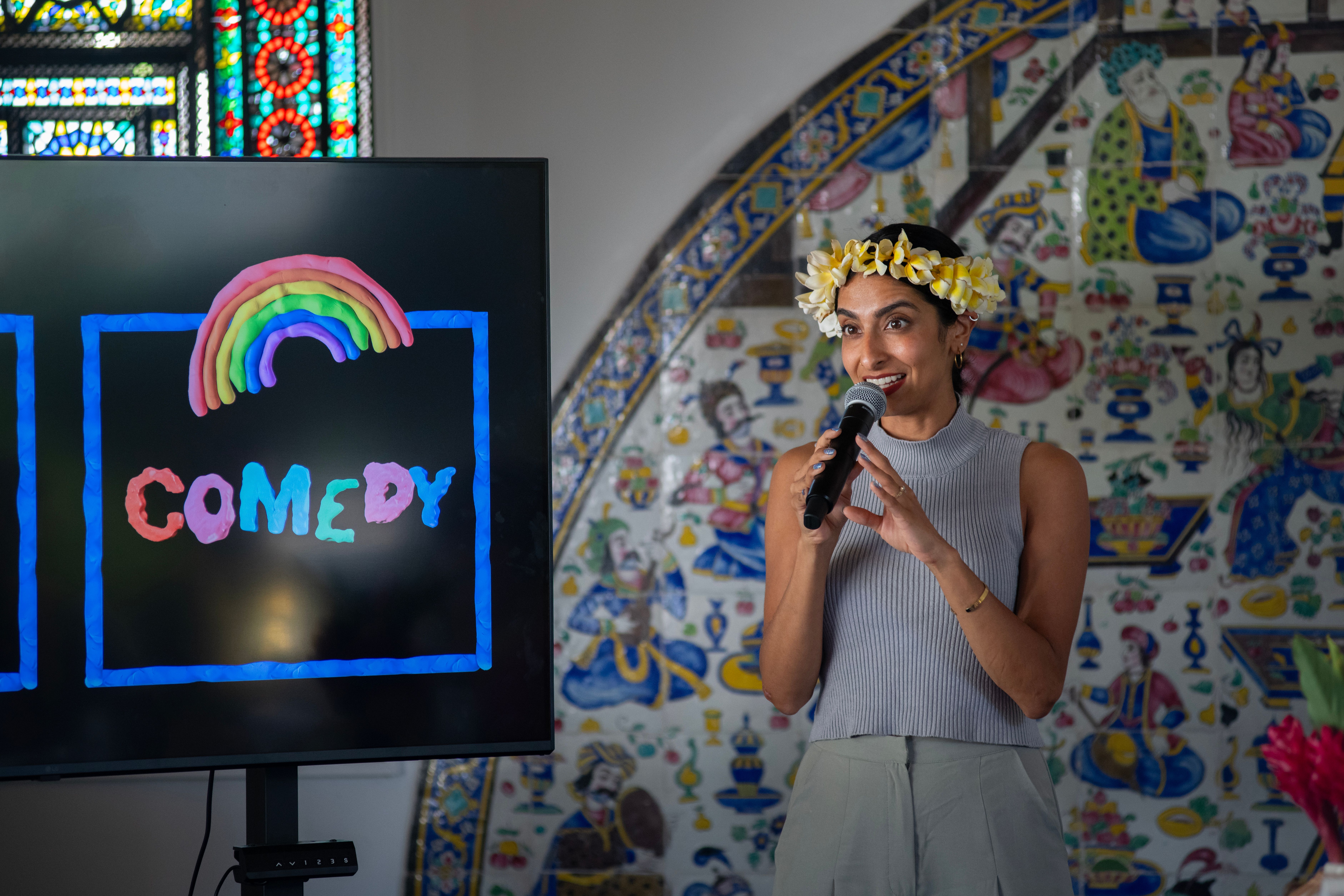 Artist holds a microphone in front of a screen with the word “COMEDY” in bright colors.