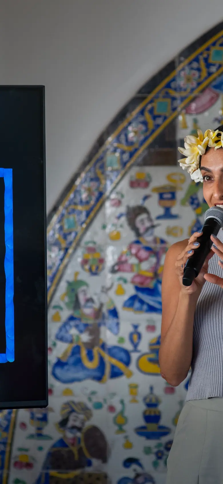 Artist holds a microphone in front of a screen with the word “COMEDY” in bright colors.