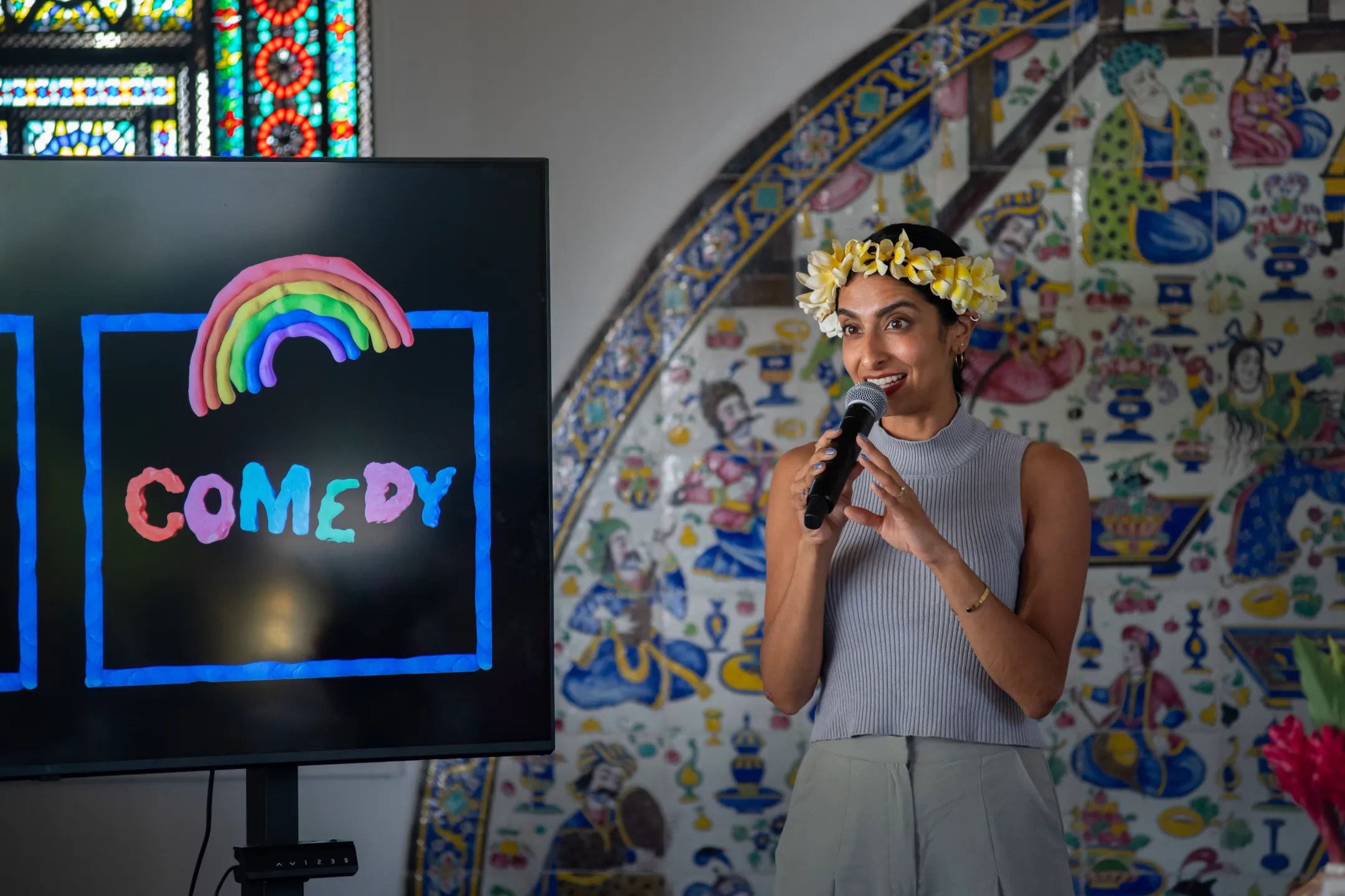Artist holds a microphone in front of a screen with the word “COMEDY” in bright colors.