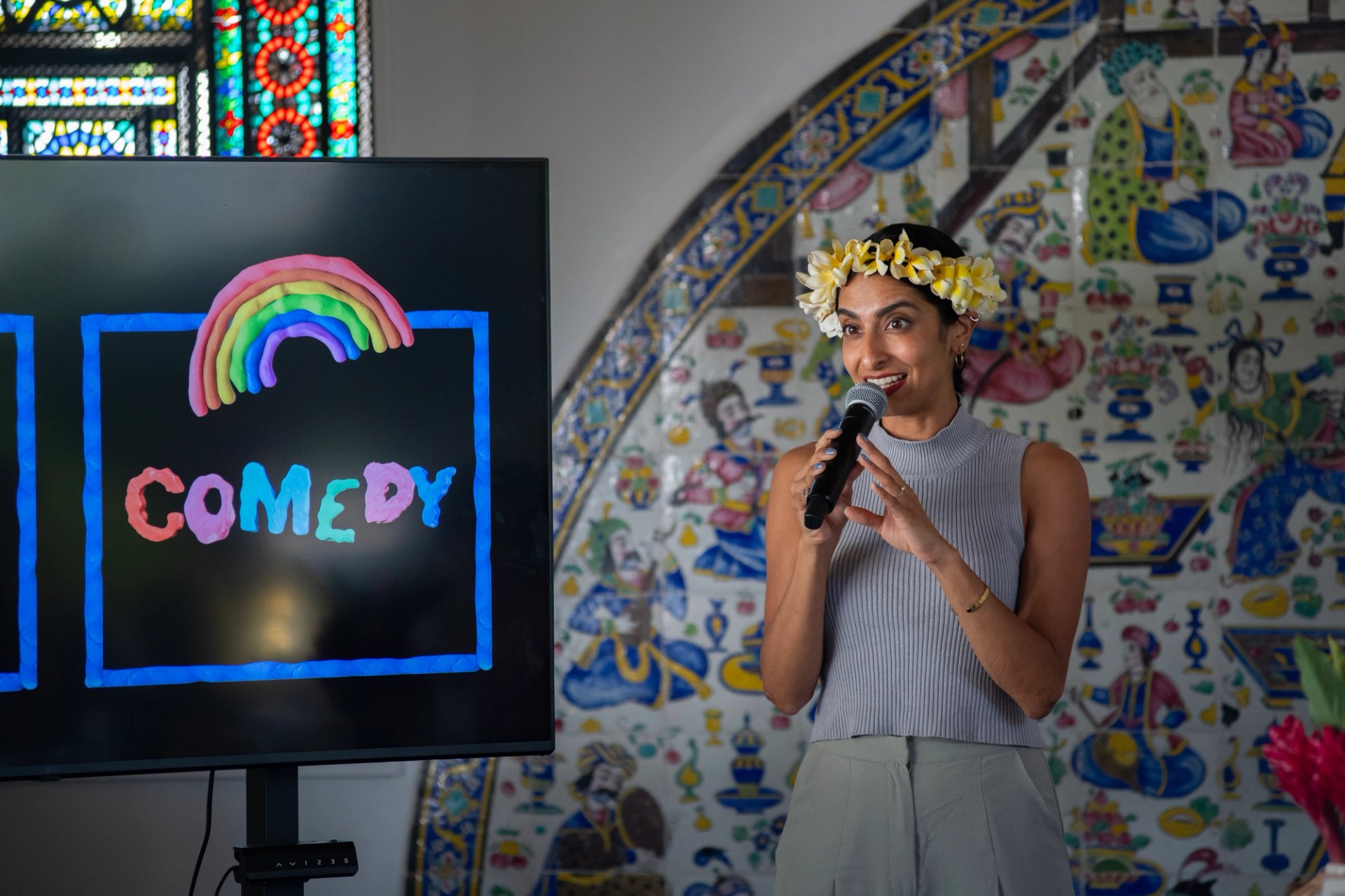Artist holds a microphone in front of a screen with the word “COMEDY” in bright colors.